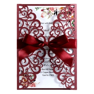 Detail of laser-cut burgundy wedding invitation with elegant floral inner card and red ribbon