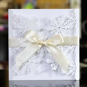 Detail of laser-cut white snowflake invitation card with cream satin ribbon bow