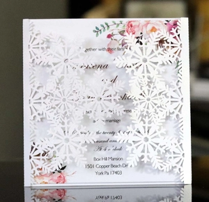 Macro view of laser-cut white snowflake invitation with floral card detail and precision carving