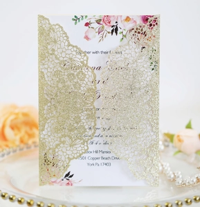 Detail of laser-cut gold glitter wedding invitation with floral card and pearl accents