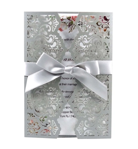 Close-up of laser-cut floral wedding invitation with elegant silver silk ribbon bow