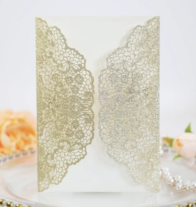 Detail of laser-cut glitter gold wedding invitation with lace floral texture and pearls