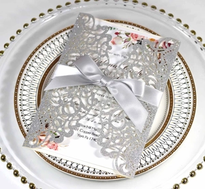Detail of silver glitter laser-cut wedding invitation with bow and floral inner card