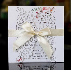 Detailed laser-cut wedding invitation featuring a floral inner card and white ribbon bow