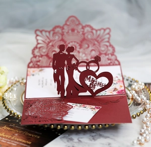 Detail of laser-cut burgundy wedding invitation featuring Mr & Mrs motif and rings