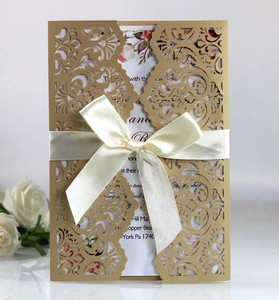 Detail of laser cut wedding invitation with cream satin bow and gold floral inner card