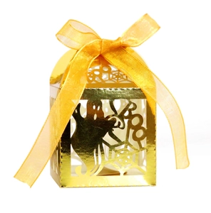 Close-up of golden laser-cut Halloween favor box with ghost pattern and yellow ribbon