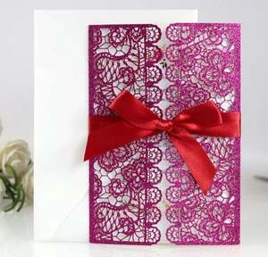 Detail of rose gold glitter laser-cut lace wedding invitation with a red satin bow and envelope