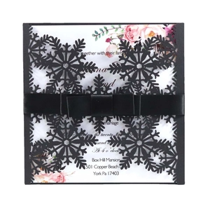 Detail of square laser-cut snowflake invitation with black silk ribbon bow and rose print