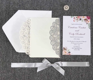 Détail d'invitation de mariage découpée au laser argentée avec ruban et broche en perle