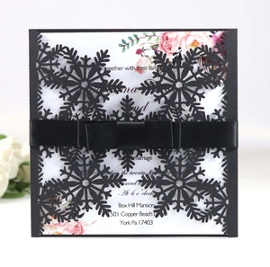 Elegant laser-cut black snowflake wedding invitation with white floral card and satin ribbon