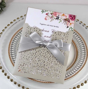 Close-up of laser-cut wedding invitation with champagne gold sleeve and grey silk bow