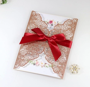 Detail of laser-cut glitter invitation with floral insert and burgundy ribbon bow