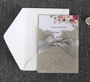 Detail of laser-cut wedding invitation with champagne lace sleeve and silk ribbon bow