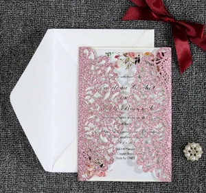 Close-up of laser-cut glitter wedding invitation with floral insert and red ribbon