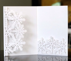 Close-up of laser-cut snowflake patterns on a white festive invitation card