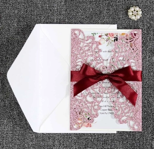 Detail of pink glitter laser-cut wedding invitation with burgundy ribbon and floral card