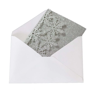 Macro detail of laser-cut snowflake invitation with silver glitter finish and white envelope