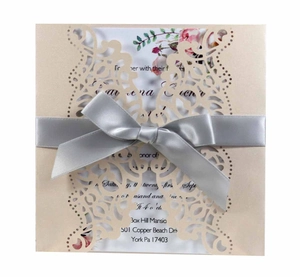 Laser-cut wedding invitation with champagne paper cover and a silver satin ribbon bow