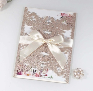 Detail of laser cut champagne gold glitter wedding invitation with white silk bow accent