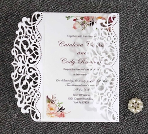 Detail of laser-cut white wedding invitation with floral insert and pearl brooch