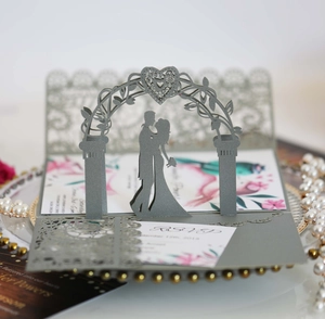 Intricate laser-cut 3D wedding invitation featuring a gray silhouette of a couple in a floral arch