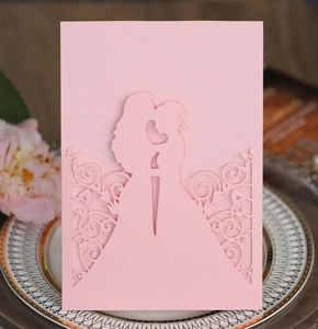 Detail of pink laser-cut wedding invitation featuring a romantic couple silhouette and floral lace