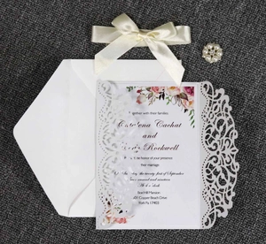 Flat lay of white laser-cut wedding invitation set with floral card and satin bow