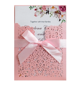 Detail of pink laser cut wedding invitation with floral pattern and satin ribbon bow