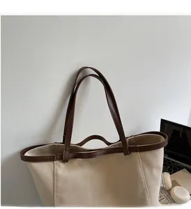 Detail of the minimalist canvas tote bag showing the brown leather handles and stitched trim