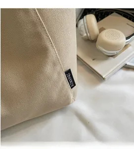 Close-up of beige canvas tote bag with black woven label detailing and textile texture