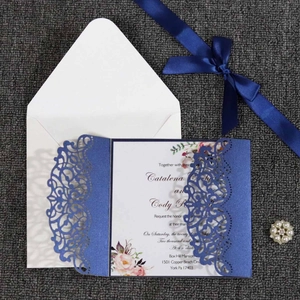 Detail of laser-cut navy wedding invitation set with floral patterns and a satin ribbon