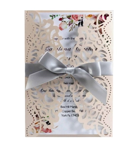 Detail of laser-cut floral wedding invitation with pink flowers and a grey satin ribbon