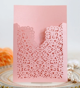 Detail of pink laser-cut wedding invitation with pearl necklace on vintage porcelain plate