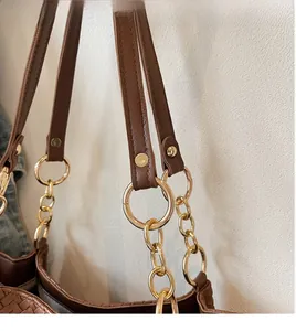 Detailed close-up of brown woven tote bag with gold chain strap and polished hardware