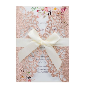 Close-up of rose gold glitter laser-cut wedding invitation with white silk ribbon bow