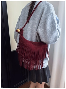 Detailed view of burgundy fringe crossbody bag with wooden bead shoulder strap on a model