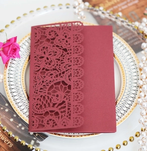 Macro detail of wine red laser cut lace wedding invitation card on elegant dinner plate