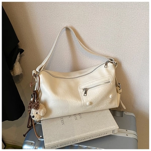Detail of cream leather shoulder bag with decorative front pocket and cute bear charm