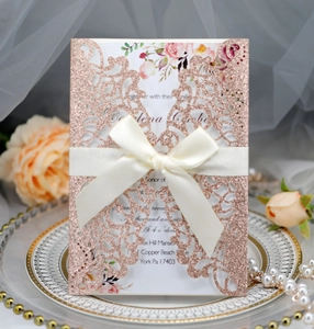 Detail of rose gold glitter laser-cut invitation with cream ribbon bow on decorative plate