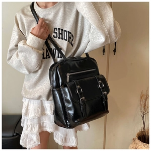 Detail of glossy black oil leather backpack featuring metal buckle and zipper closure