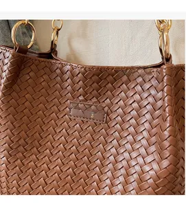Detail of brown woven tote bag showing checkerboard texture and golden metal rings