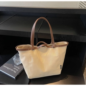 Close-up of minimalist canvas tote bag with brown leather trim and side brand label detail
