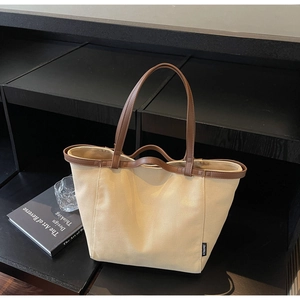 Minimalist canvas tote bag with brown leather handles and side label on display