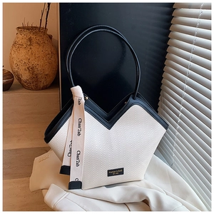 Detail of minimalist woven tote bag featuring black leather trim and decorative ribbon