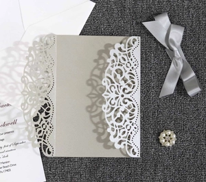 Macro shot of white laser-cut floral wedding invitation with silver ribbon and pearl accent