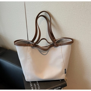 Detail of canvas tote bag with brown trim placed on a leather sofa and design book