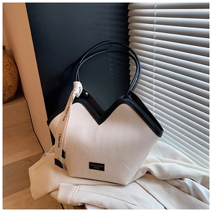 Detail of cream tote bag with black trim, V-shaped opening and decorative ribbon accent