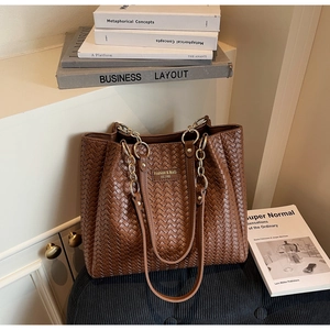 Détail du sac cabas tressé marron avec bandoulière en chaîne et texture cuir de luxe