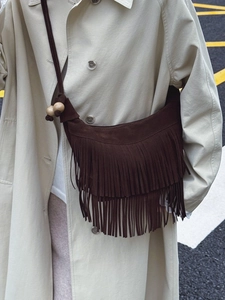 Sac demi-lune en daim marron avec franges et perles en bois porté à l'épaule par un mannequin